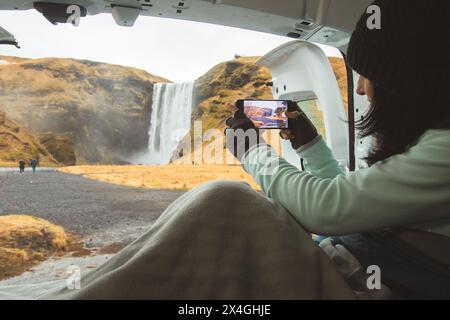 Femme voyageuse tirer une photo vidéo de belle cascade utiliser smartphone. Touriste féminine prend des photos avec l'appareil photo de téléphone portable lors d'un voyage en islandais Banque D'Images