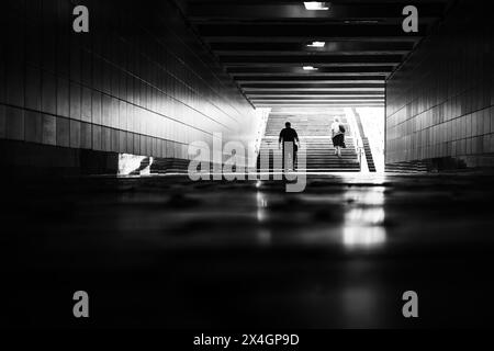 Vue arrière des gens dans le passage souterrain de la ville. Sortez du métro. Photo de rue en noir et blanc. Scène urbaine typique. Fond monochrome abstrait Banque D'Images