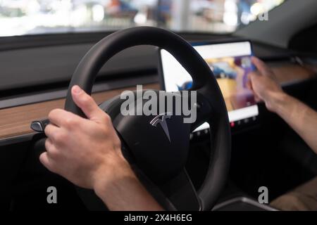 Derrière le volant Tesla modèle y voiture électrique, mains masculines sur la colonne du conducteur, voiture de tourisme moderne, présentant des caractéristiques intérieures telles que la roue de contrôle Banque D'Images