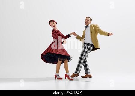 Jeune homme et femme, couple habillé dans des tenues d'inspiration rétro dansant joyeusement ensemble isolé sur fond blanc de studio Banque D'Images