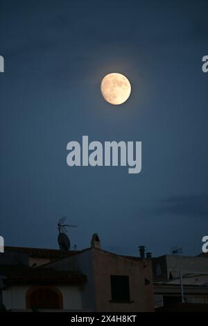 une pleine lune brillante brille sur les toits, projetant une lueur sereine dans le ciel nocturne tranquille, créant une atmosphère paisible et tranquille dans l'obscurité Banque D'Images