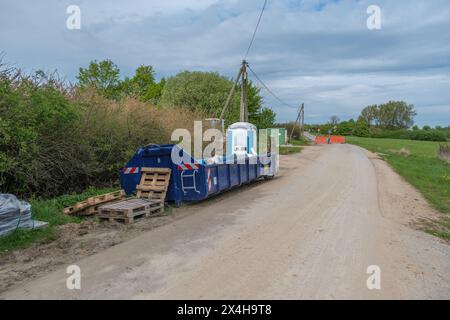 à côté d'une route se trouve un grand conteneur bleu pour les déchets de construction et une toilette de chantier Banque D'Images