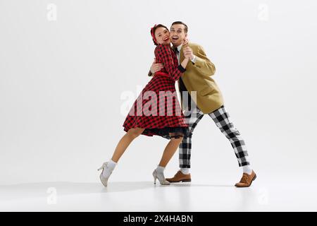 Élégant, charmant jeune couple, homme et femme dans des vêtements de style rétro dansant isolé sur fond blanc de studio Banque D'Images