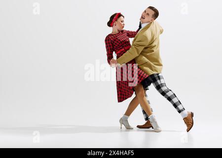 Élégant, charmant jeune couple, homme et femme dans des vêtements de style rétro dansant isolé sur fond blanc de studio Banque D'Images