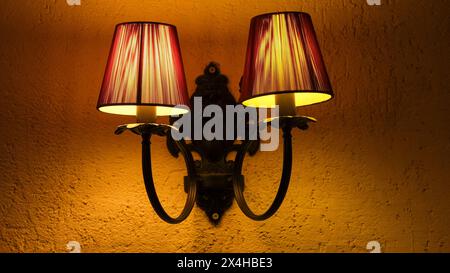 Gros plan sur une lampe murale double vintage ornée de ferronnerie. Les deux abat-jour sont chaleureusement éclairés, créant une atmosphère chaleureuse et accueillante. Banque D'Images