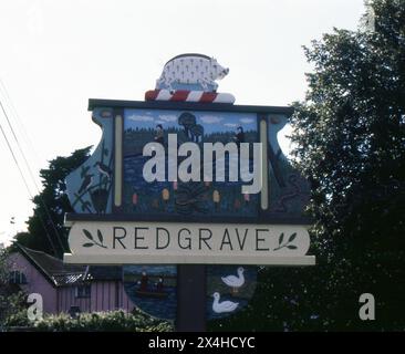 Suffolk. 1987 – photographie du signe du village de Redgrave dans le Suffolk, en Angleterre. Le panneau est fabriqué à la main à partir de bois sculpté et décoré avec des repères et des motifs locaux. Redgrave est situé à environ 4,5 miles à l'ouest de la ville de Diss, et juste au sud de la rivière Waveney qui forme la frontière du comté avec Norfolk. Banque D'Images