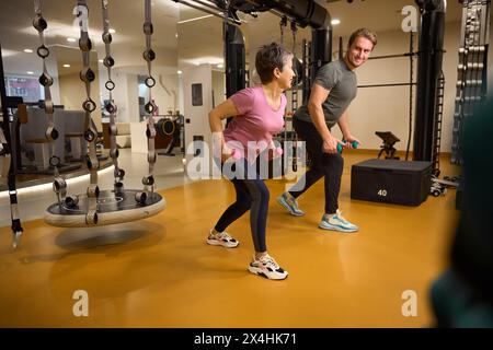 Entraîneur masculin souriant et femme adulte faisant de l'exercice sportif avec des haltères Banque D'Images