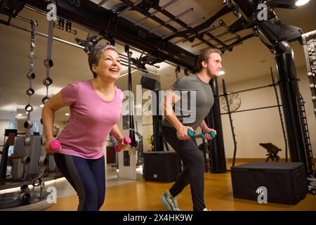 Entraîneur enseignant femme souriante mature faisant de l'exercice sportif avec des haltères dans le gymnase Banque D'Images