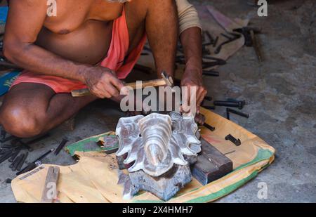 Un artisan indien qualifié travaille méticuleusement sur une forme métallique pour créer une statue d'un Dieu hindou Banque D'Images