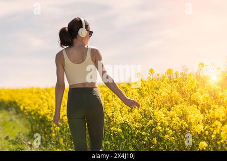 Femme sportive marchant dans la campagne à travers un champ jaune, vue arrière. Banque D'Images