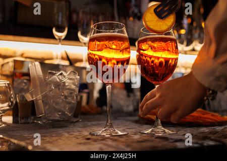 BarTender prépare deux verres de cocktail Aperol spritz sur le comptoir du bar, ajoute des tranches d'orange fraîches. Boisson italienne alcoolisée typique, apéritif fait avec Banque D'Images