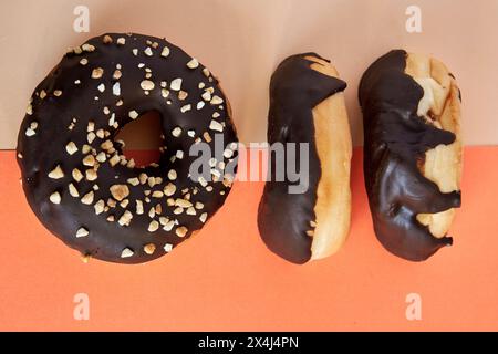 3 beignet recouvert de chocolat avec des noix à écraser sur le dessus sur fond orange et beige. Banque D'Images