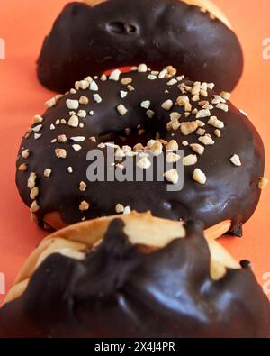 Trois beignets recouverts de chocolat avec des noix écrasées sur le dessus sur fond orange Banque D'Images