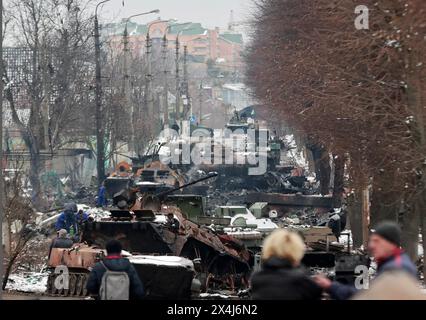 Les gens regardent les restes vidés de véhicules militaires russes sur une route dans la ville de Bucha, près de la capitale Kiev, Ukraine, mardi 1er mars 2022. Banque D'Images