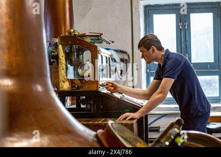 ISLAY, ÉCOSSE -Kilchoman whisky distillerie encore homme vérifie les niveaux d'alcool dans le Spirit Safe. Banque D'Images