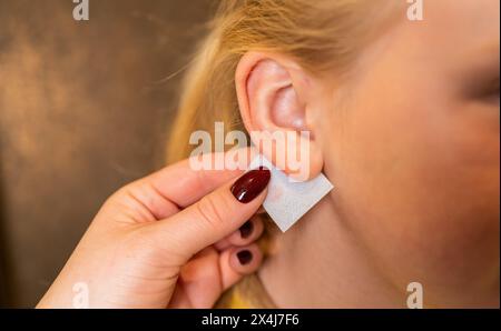 main d'un travailleur médical professionnel appliquant une lingette désinfectante sur le lobe de l'oreille d'une jeune fille avant perçage d'oreille dans un magasin de bijoux Banque D'Images