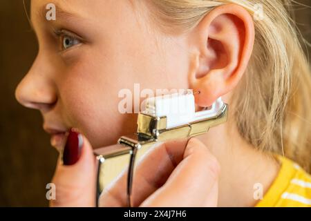 Fille se faisant percer l'oreille avec un pistolet de perçage et des ongles rouges visibles dans une bijouterie Banque D'Images