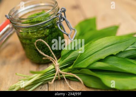 Gros plan du pesto à l'ail sauvage dans un bocal en verre ouvert avec des feuilles fraîches sur une surface en bois Banque D'Images