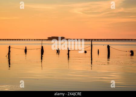 Lever de soleil d'hiver dans la baie d'Alfacs, dans le delta de l'Èbre, avec mer calme et fermes de moules en arrière-plan (Tarragone, Catalogne, Espagne) Banque D'Images