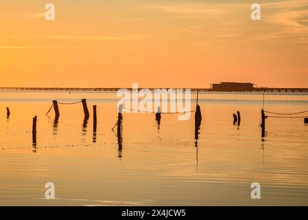 Lever de soleil d'hiver dans la baie d'Alfacs, dans le delta de l'Èbre, avec mer calme et fermes de moules en arrière-plan (Tarragone, Catalogne, Espagne) Banque D'Images