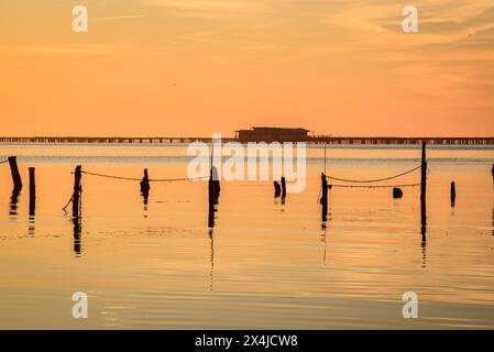 Lever de soleil d'hiver dans la baie d'Alfacs, dans le delta de l'Èbre, avec mer calme et fermes de moules en arrière-plan (Tarragone, Catalogne, Espagne) Banque D'Images