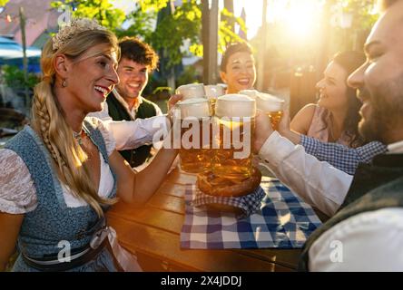 Groupe d'amis toast avec des tasses à bière dans le jardin de bière en plein air ou oktoberfest en Bavière, Allemagne, lumière du soleil, bretzel sur tissu à carreaux Banque D'Images
