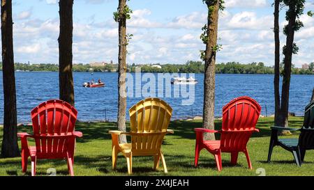 Chaises adirondack colorées sur l'herbe verte près de la rive du magnifique lac Irving à Bemidj Minnesota par une journée ensoleillée. Bateaux sur l'eau, et Banque D'Images