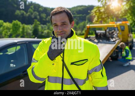 Opérateur de dépanneuse parlant sur un talkie-walkie regardant la caméra pour charger une voiture endommagée sur une dépanneuse. Banque D'Images