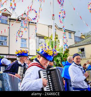 Un joueur d'accordéon Blue Ribbon porte un chapeau avec des cloches bleues et des cowslips pour le festival 'Obby 'Oss', un événement folklorique annuel le jour de mai à Padstow, Cornouailles Banque D'Images