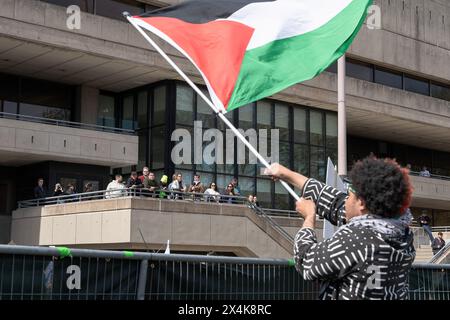 Un manifestant du campement agite un drapeau palestinien tandis que les gens qui surplombent le campement surveillent le rassemblement. Des centaines de personnes ont assisté à un rassemblement pro-israélien organisé par la section de Nouvelle-Angleterre du Conseil israélien américain sur les marches de l'entrée du MIT sur Massachusetts Avenue. Le rassemblement était l'une des plus grandes contre-manifestations organisées près d'une manifestation de campement universitaire de la région de Boston. Le rassemblement était à environ 30 à 40 mètres du campement pro-palestinien sur le campus du MIT. La présence de la police était élevée dans la zone et des barricades métalliques avaient été placées pour empêcher les deux parties de tout affrontement. Quelques partisans israéliens Banque D'Images