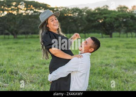 homme latin brun aux cheveux foncés essayant fort de soulever sa petite amie pendant qu'elle sourit de rire Banque D'Images