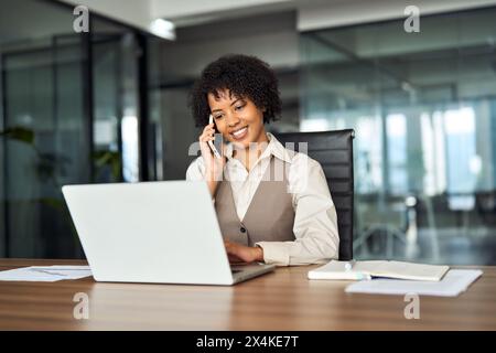 Heureuse femme d'affaires afro-américaine faisant appel parlant au téléphone au travail. Banque D'Images