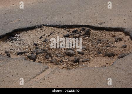 Un grand nid de poule dans la rue de la ville crée des conditions de conduite dangereuses pour les véhicules qui passent. Une route asphaltée délabrée Banque D'Images