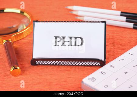 Word PhD. Docteur en philosophie. DOCTORAT sur une carte de visite blanche dans un stand avec une loupe, des crayons et une calculatrice Banque D'Images