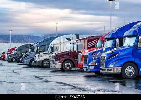 Transporteurs industriels différents tracteurs de semi-remorques de grande taille avec semi-remorques chargées debout en rangée sur le parking d'arrêt de camion à l'heure du matin tak Banque D'Images