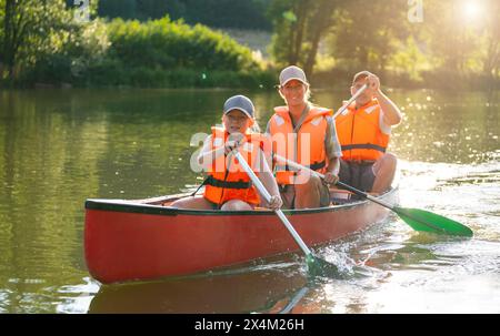 Heureuse famille de trois canoës sur une rivière, avec la lumière du soleil se reflétant sur l'eau autour d'eux en été. Famille en kayak. Nature sauvage et fu de l'eau Banque D'Images