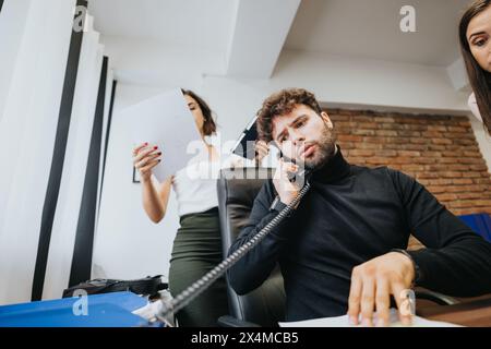 Des collègues concentrés sur le dépannage dans un environnement de bureau, avec une femme pointant vers un écran d'ordinateur et un homme utilisant un téléphone. Banque D'Images