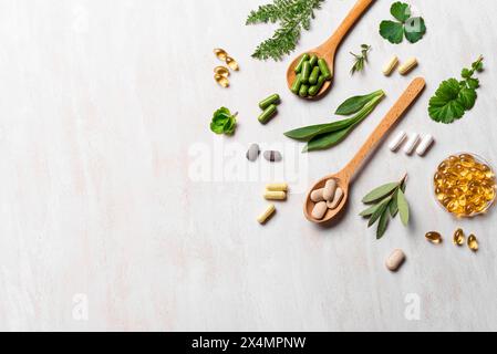 Vitamines naturelles, suppléments à base de plantes et feuilles vertes sur fond de bois blanc, vue de dessus, espace de copie. Diverses capsules et pilules biologiques. Banque D'Images