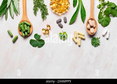 Vitamines naturelles, suppléments à base de plantes et feuilles vertes sur fond de bois blanc, vue de dessus, espace de copie. Diverses capsules et pilules biologiques. Banque D'Images