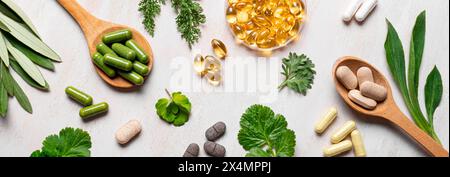 Vitamines naturelles, suppléments à base de plantes et feuilles vertes plates reposent sur fond de bois blanc. Diverses capsules et pilules biologiques, bannière. Banque D'Images