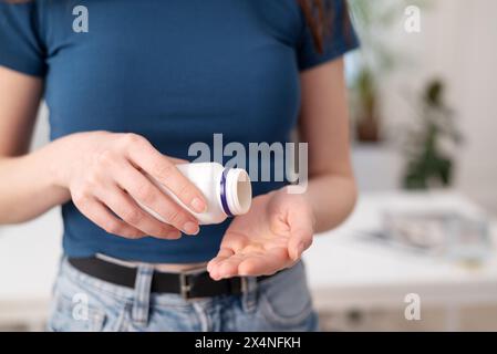 Jeune femme tient des capsules dans une main, femelle prend des suppléments et des vitamines d'une bouteille, vue rapprochée. Banque D'Images