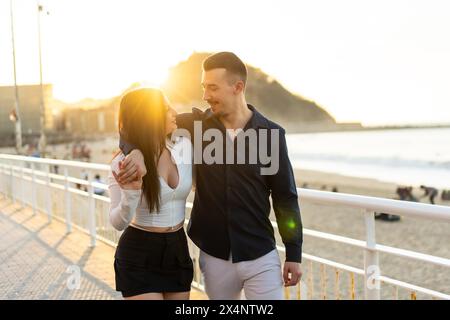 Romantique jeune couple embrassant à côté de la mer tout en se promenant le long d'une promenade Banque D'Images