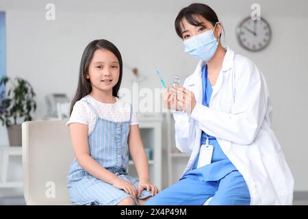 Médecin féminin avec seringue et ampoule vaccinant la petite fille asiatique en clinique Banque D'Images