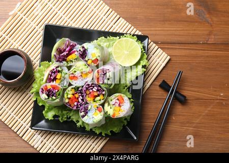 Délicieux rouleaux de printemps, sauce soja et baguettes sur table en bois, vue de dessus Banque D'Images