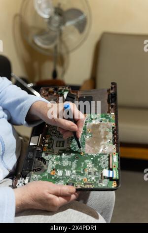 Vieille femme avec un ordinateur portable sur ses genoux et un tournevis essayant de le réparer elle-même, amateur de bricolage économisant des coûts Banque D'Images