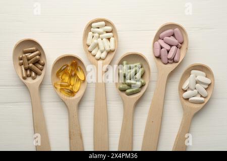 Différentes capsules de vitamines dans des cuillères sur une table en bois blanc, pose à plat Banque D'Images