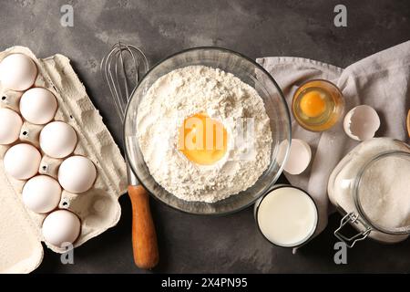 Faire de la pâte. Farine avec jaune d'oeuf dans un bol et d'autres produits sur une table texturée grise, pose à plat Banque D'Images