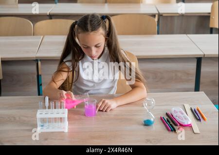 Une écolière conduit des expériences dans une leçon de chimie. Fille versant des liquides colorés dans un bol. Banque D'Images