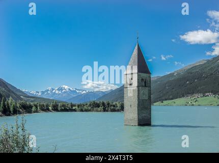 Une tour pittoresque se trouve au milieu d'un lac tranquille, entourée de montagnes majestueuses sous un ciel rempli de nuages moelleux. Un naturel époustouflant Banque D'Images