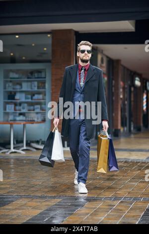 Homme, sacs à provisions et vêtements formels au centre commercial, marche et client ou acheteur, rabais et vente au détail. Boutique, vente et virée dans les lunettes de soleil, costume et Banque D'Images